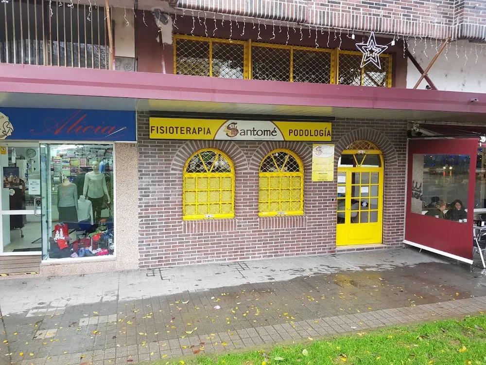 Fachada de la clínica en la Praza Eugenio Fadrique: bajo de ladrillo con ventanas y puerta amarillas y rótulo Fisioterapia Santomé Podología (foto del centro)